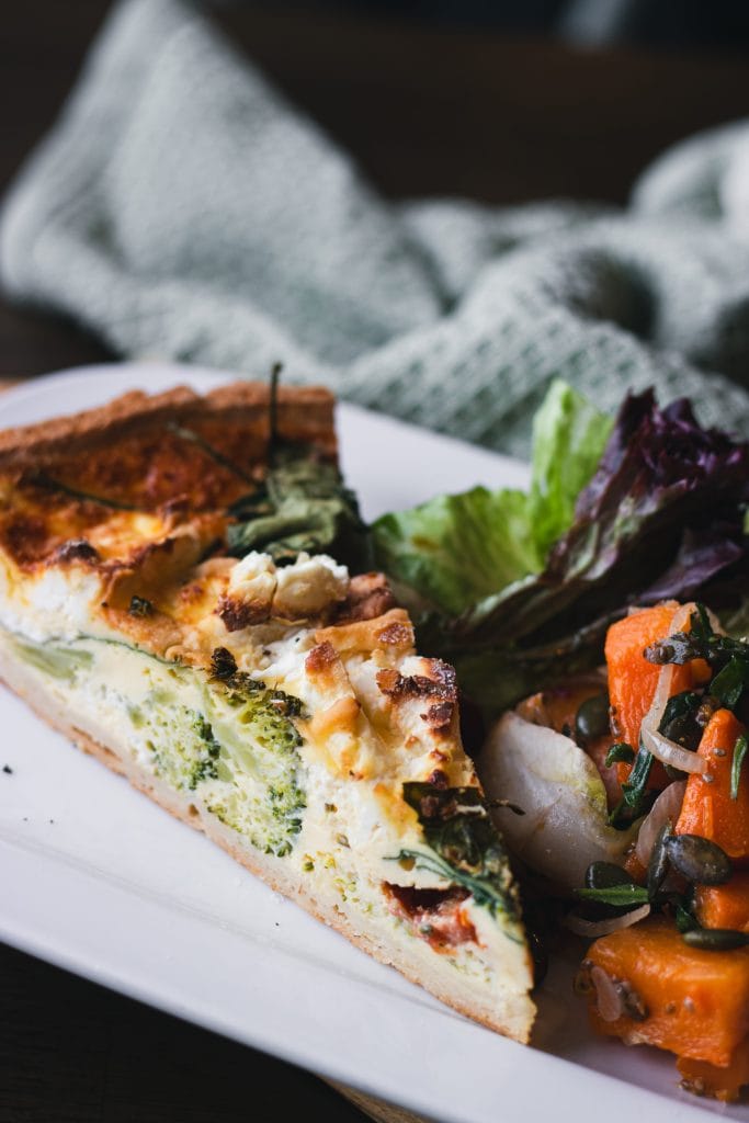 Slice of savoury tart served with fresh salad and roasted vegetables